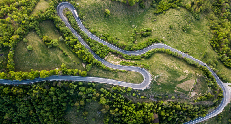 Aerial view of a winding mountain road surrounded by greenery, illustrating the Pegasus TRK Evo’s use in road infrastructure surveys, including pre-construction assessments, progress monitoring, and pavement condition analysis.